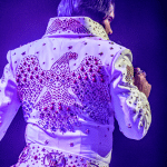 Elvis impersonator JD King on stage in white Aloha Eagle jumpsuit