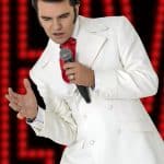 Elvis impersonator JD King dressed in white in front of a red neon sign