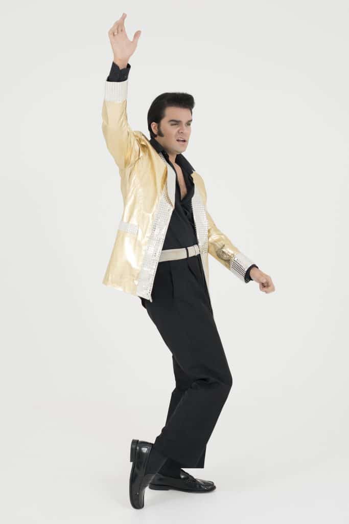Elvis impersonator JD King wearing a gold jacket in a dancing pose with arm raised in the air