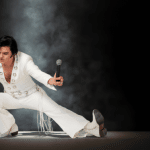 Elvis impersonator JD King leaning in spotlight wearing white