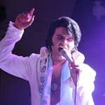 Elvis impersonator JD King on stage singing in white jumpsuit