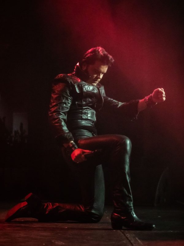 Elvis impersonator JD King kneeling on stage in black leather